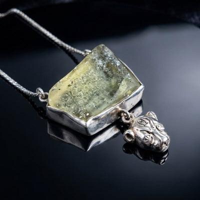 The Sekhmet Talisman — raw pale green Libyan desert glass pendant above the lioness Sekhmet, on a hand-forged silver chain