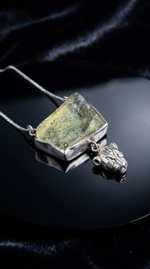 The Sekhmet Talisman — raw pale green Libyan desert glass pendant above the lioness Sekhmet, on a hand-forged silver chain