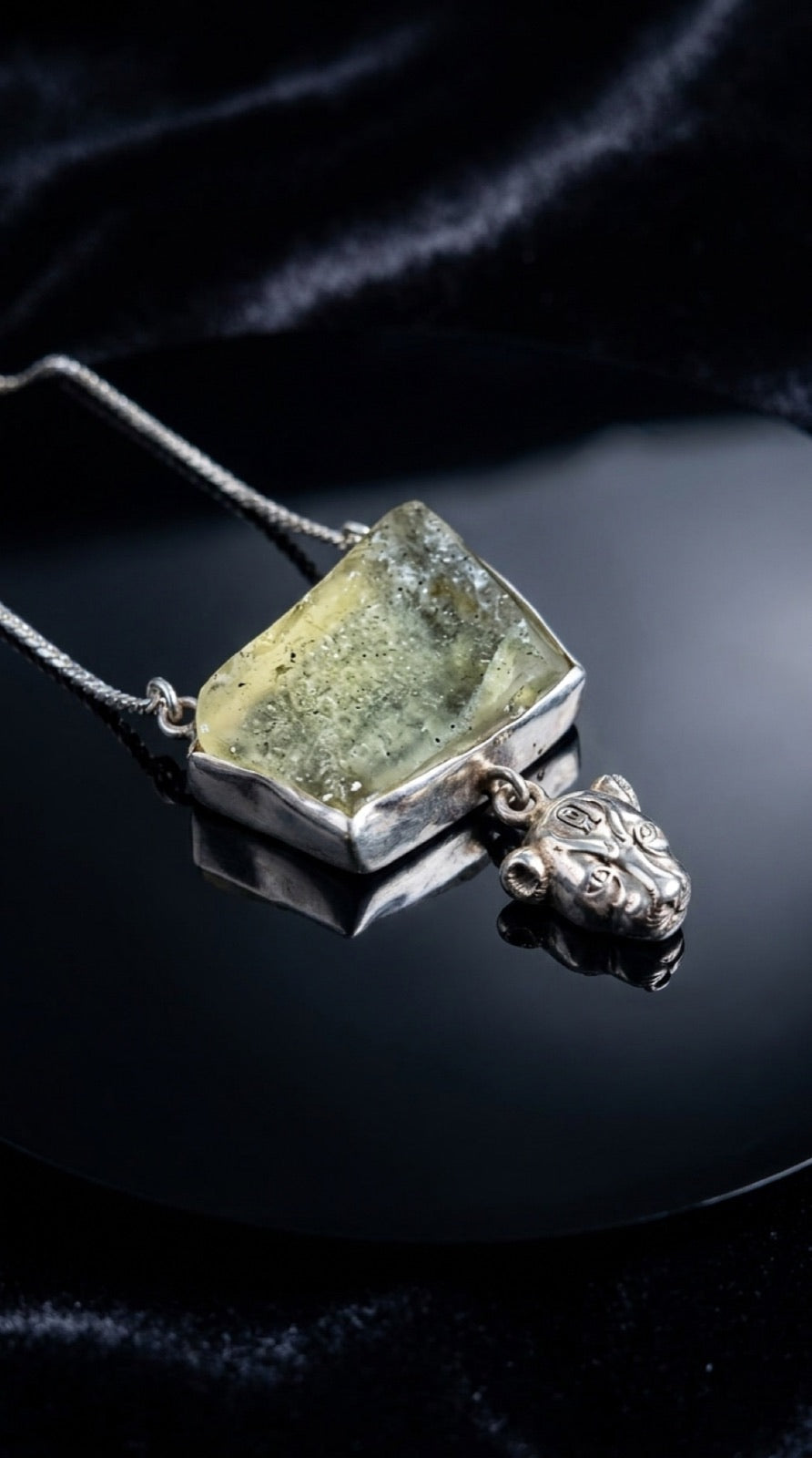 A raw shard of pale green Libyan desert glass, hand-set in silver above the lioness Sekhmet